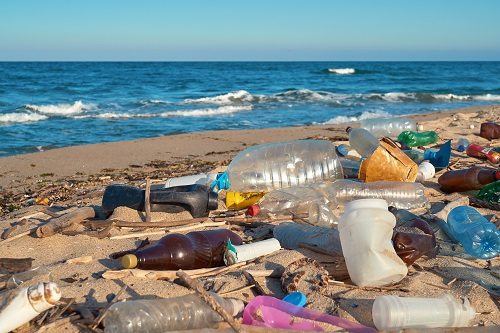 Spilled garbage on the beach of the big city. Empty used dirty plastic bottles. Dirty sea sandy shore the Black Sea. Environmental pollution. Ecological problem. Bokeh moving waves in the background