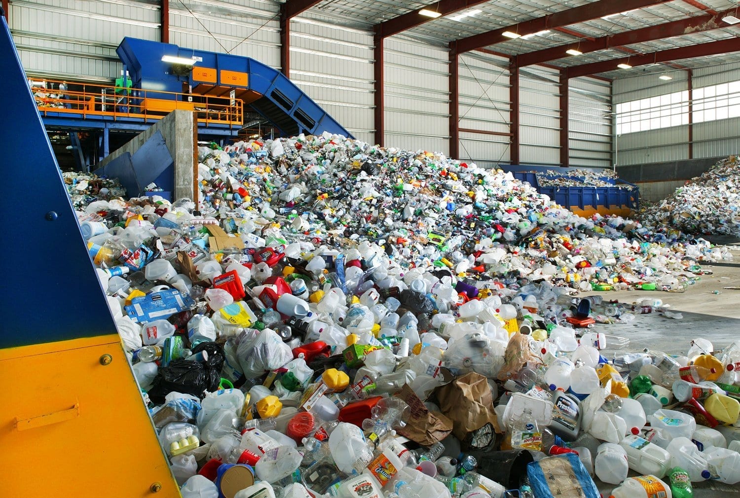 Image description: a mountain of plastic bottles fill up a large recycling facility's container